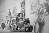 a black and white photo of a man sitting on the floor in front of paintings